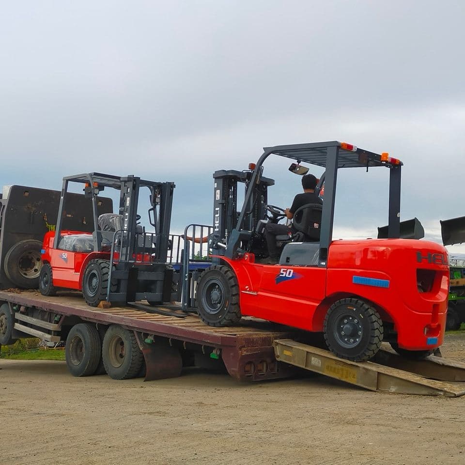 Red HELI forklifts being transported on flatbed trailer